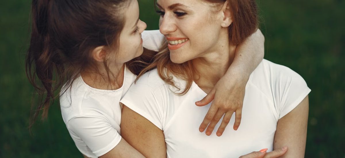 A loving mother and daughter hug in a grassy outdoor setting, sharing smiles and joy.