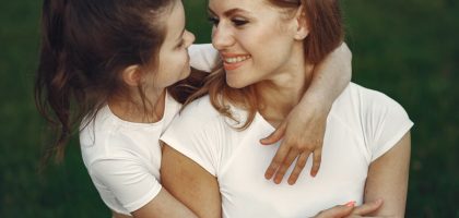 A loving mother and daughter hug in a grassy outdoor setting, sharing smiles and joy.