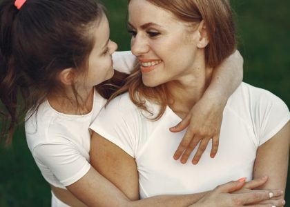 A loving mother and daughter hug in a grassy outdoor setting, sharing smiles and joy.