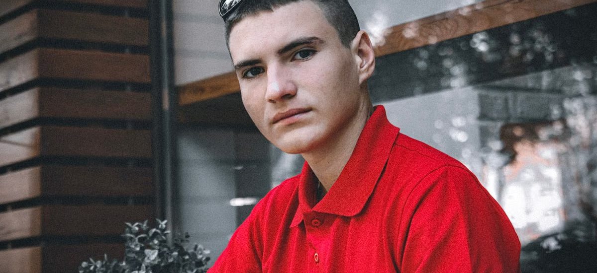 Portrait of a young man wearing a red polo shirt indoors, looking directly at the camera.