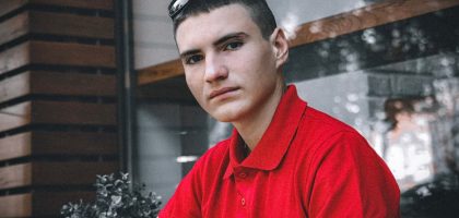 Portrait of a young man wearing a red polo shirt indoors, looking directly at the camera.