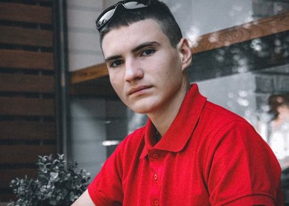 Portrait of a young man wearing a red polo shirt indoors, looking directly at the camera.